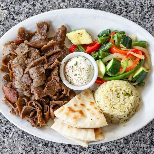 A Greek gyro platter with sliced meat, rice, pita bread, tzatziki, and sautéed vegetables.