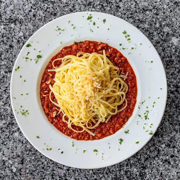 Spaghetti with red meat sauce and grated cheese, garnished with parsley on a white plate.