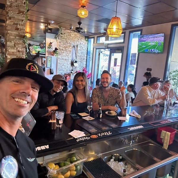 A group of friends smiling at the camera while sitting at the bar inside Demitris Taverna.