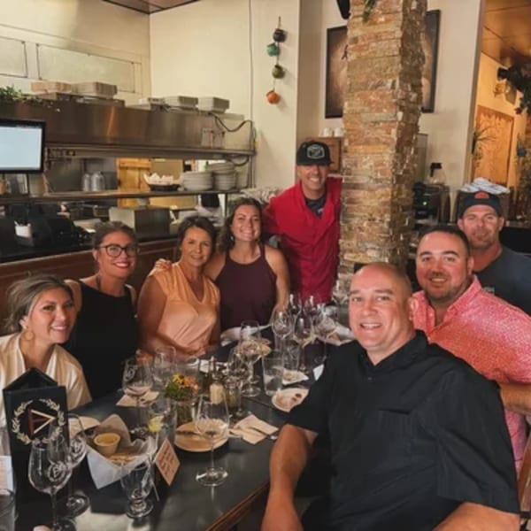 Group of eight smiling people, some staff, some guests, gathered around a table in Demitris Taverna.