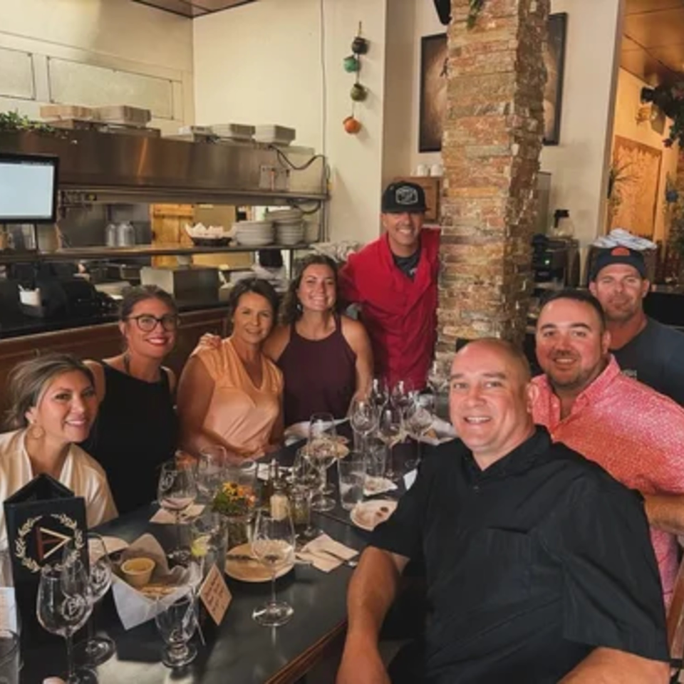 Group of eight smiling people, some staff, some guests, gathered around a table in Demitris Taverna.