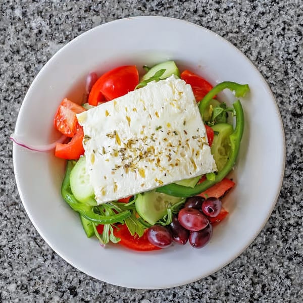A vibrant Greek salad with a large block of feta cheese, tomatoes, cucumbers, olives, and peppers.