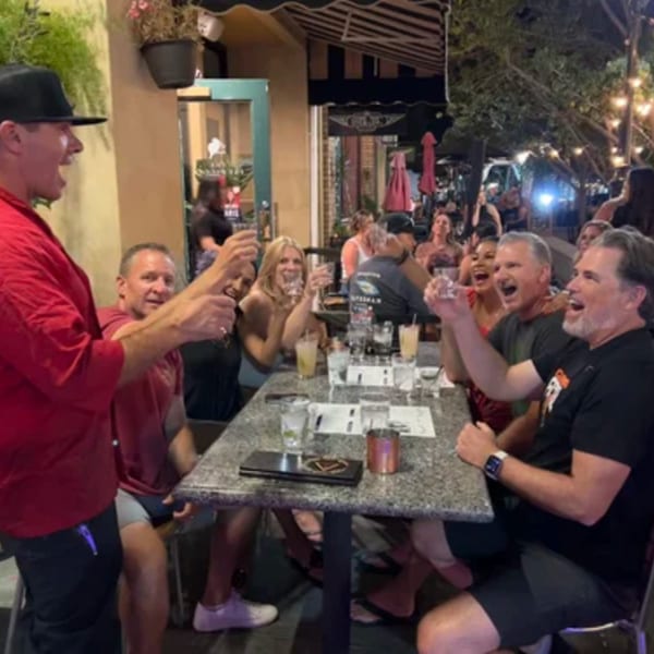 A group of happy people at Demitris Taverna raising shot glasses for a toast on an outdoor patio.