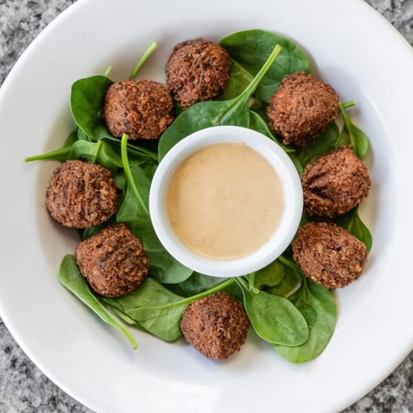 A white bowl of Demitris Taverna's falafel with spinach and a side of dipping sauce.