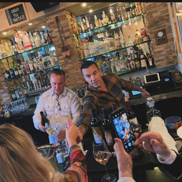 Two bartenders serving drinks to customers at Demitris Taverna, with a full bar in the background.